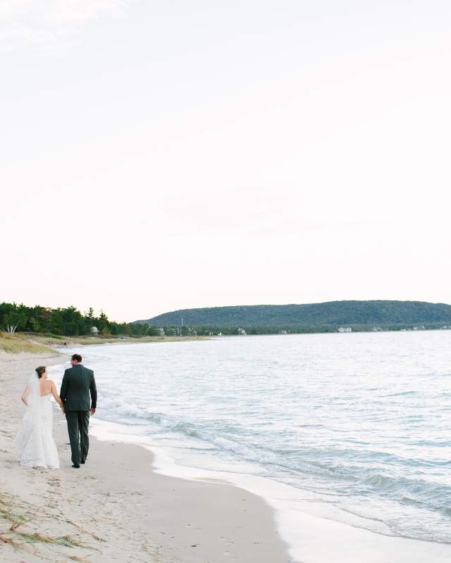 A bride and groom take a walk on the beach