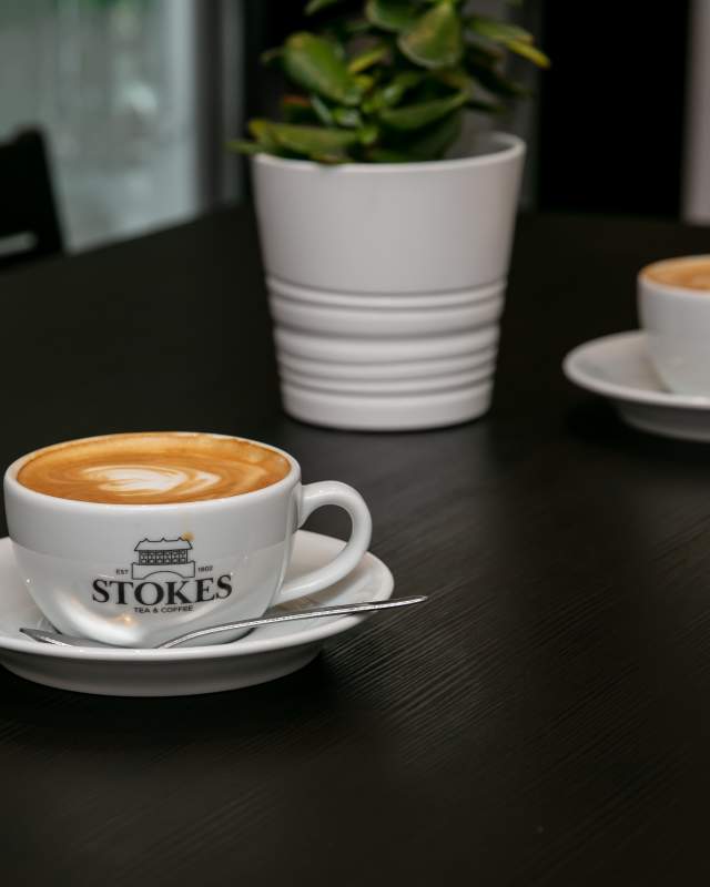 Stokes coffee mug with coffee on table with plant in background