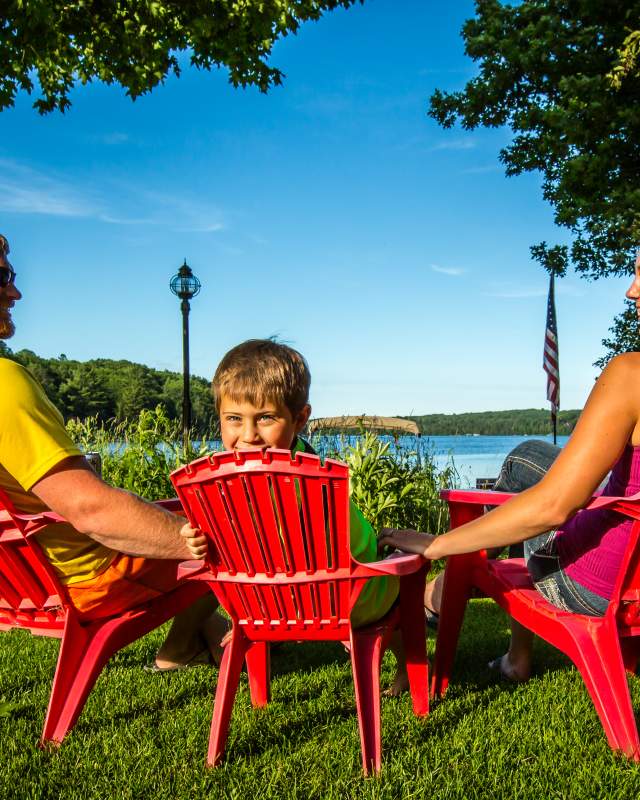 family on adirondack chairs overlooking a lake