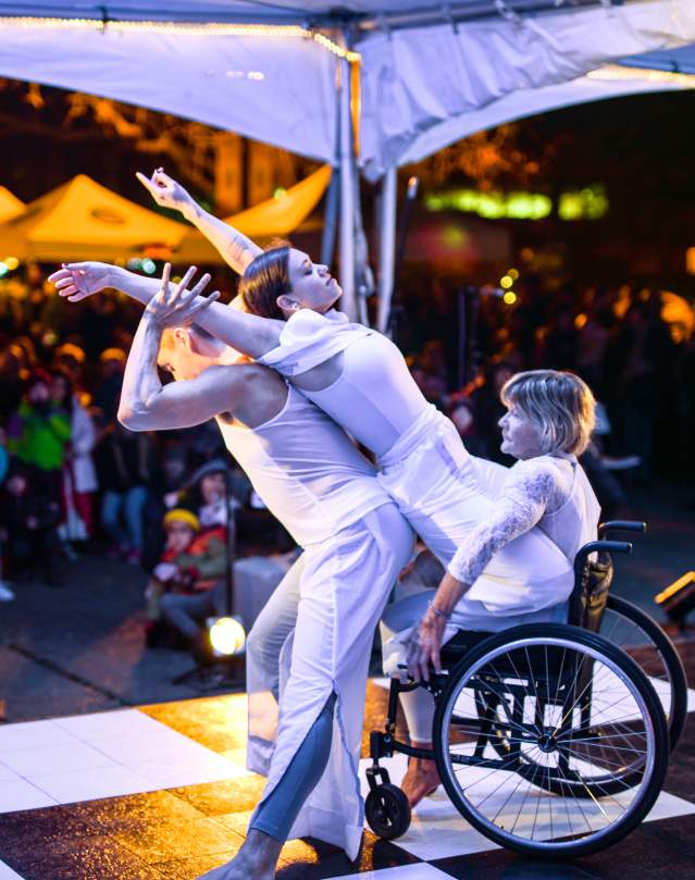Three dancers from Danceability, all dressed in white, perform on a stage in front of a crowd.