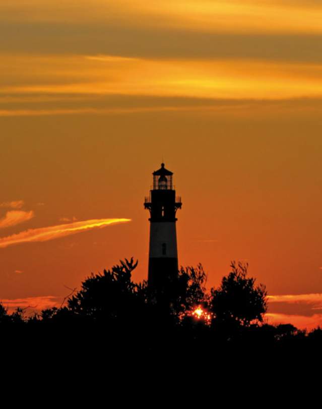 The Bodie Island Lighthouse backlit by an orange sky in Nags Head, NC