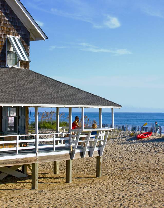 Visitors enjoy the fresh air and view from the wrap-around porch of their Outer Banks vacation rental.