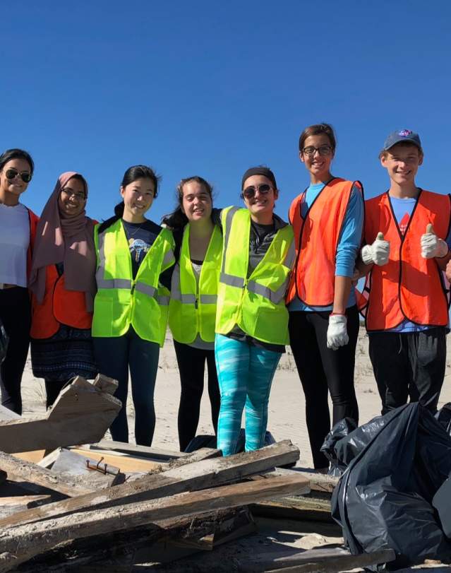 A beach clean-up crew in safety vests poses with the debris they collected on the OBX.