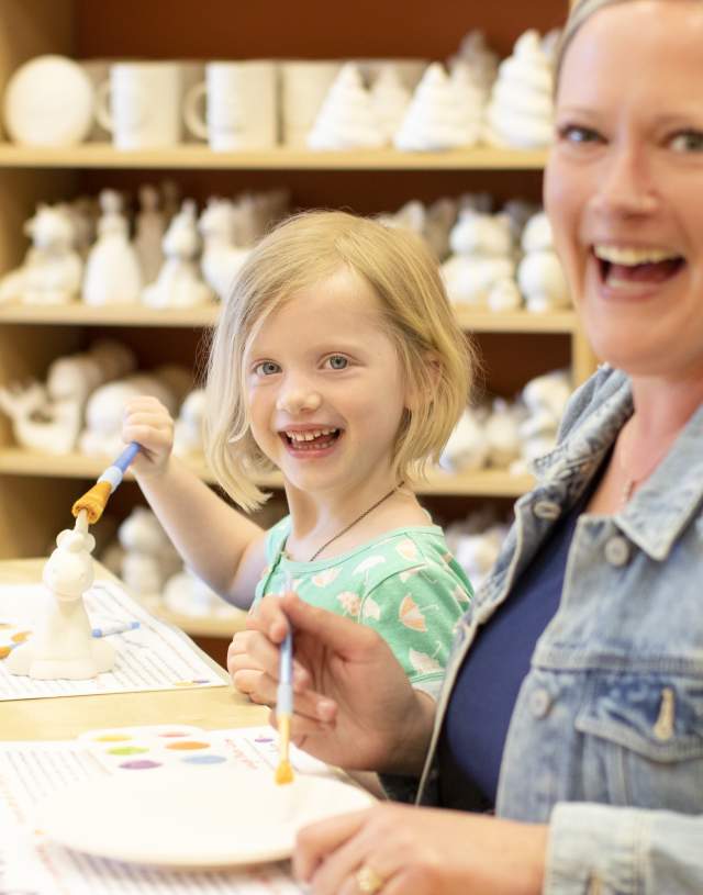 A child and woman pose smiling preparing to paint pottery at Crock a Doodle Bentonville