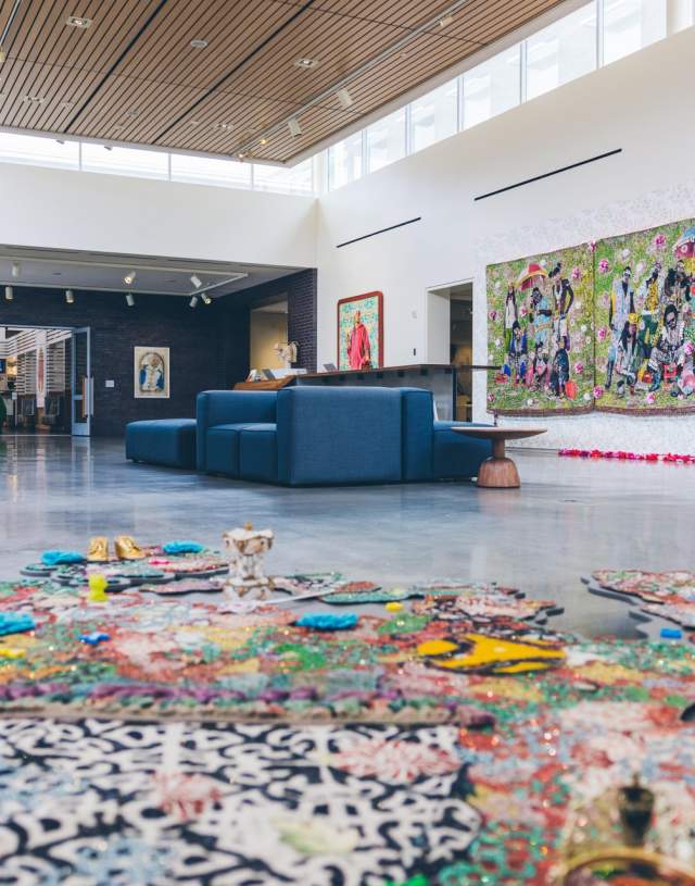 A spacious art gallery featuring vibrant wall murals and colorful floor installations. Modern seating is visible, enhancing the creative atmosphere.