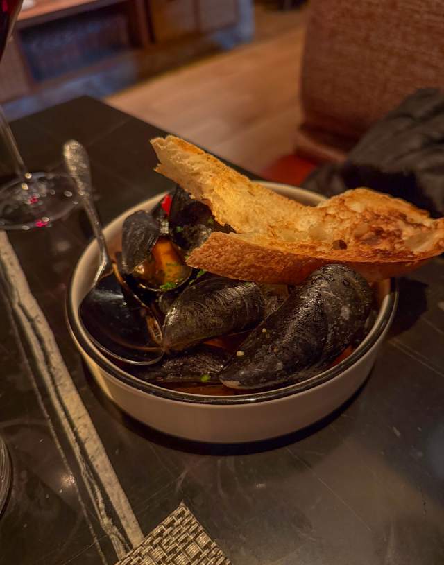 A bowl full of mussels and broth, topped with toasted bread.