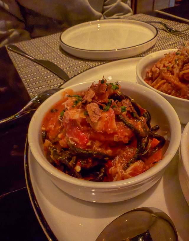 A bowl in the foreground with a heaping serving of squid ink pasta.