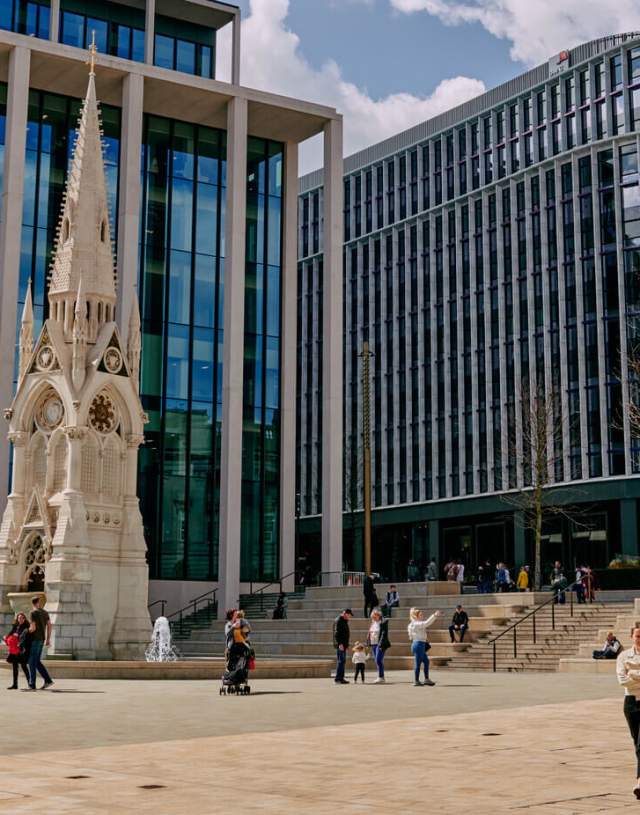 People walking around a renovated fountain in front of modern commercial buildings in Birmingham's Paradise