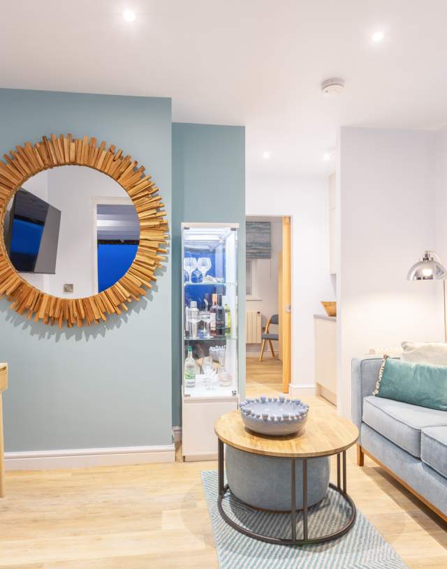A stylish living room showcases a blue couch and a large mirror reflecting the space.