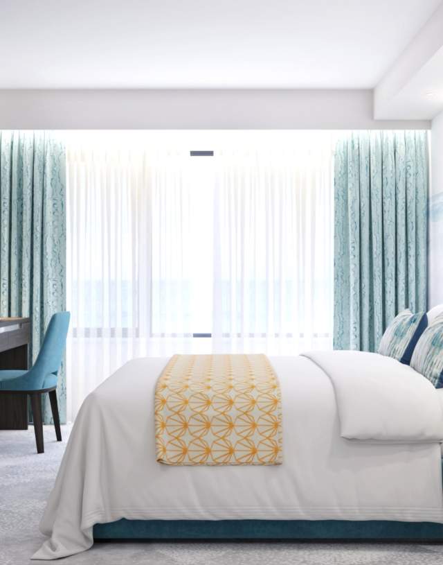 Modern hotel room with a teal upholstered bed, white linens, and a yellow patterned throw. A desk and chair sit beside a large window with teal drapes.