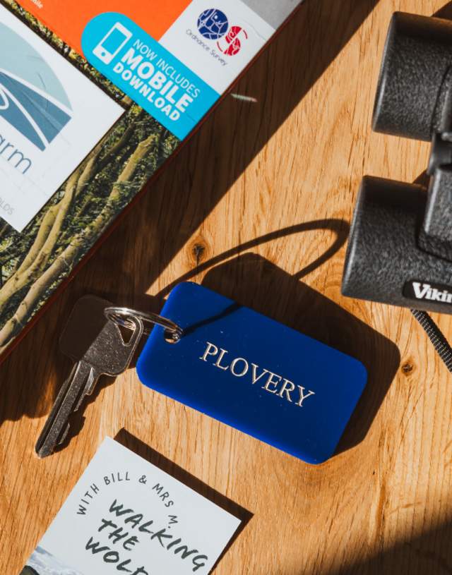 An overhead shot of the table, including an OS map, pair of black binoculars, Plovery room tag and key, and Church Farm/ Walking the Wolds business cards.