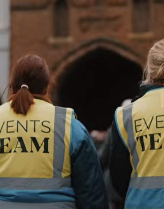 The back of two people walking towards North Bar, wearing hi vis jackets reading 'Events Team' on the back.