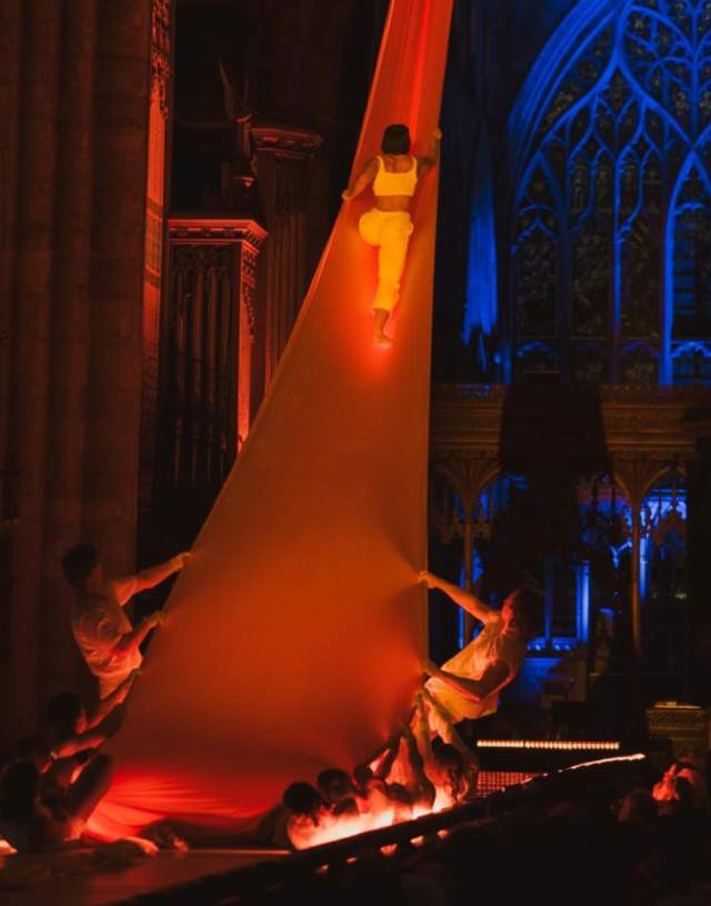 An event during Freedom Festival in Hull Minster with a dancer climbing up a long sheet held by 2 other performers