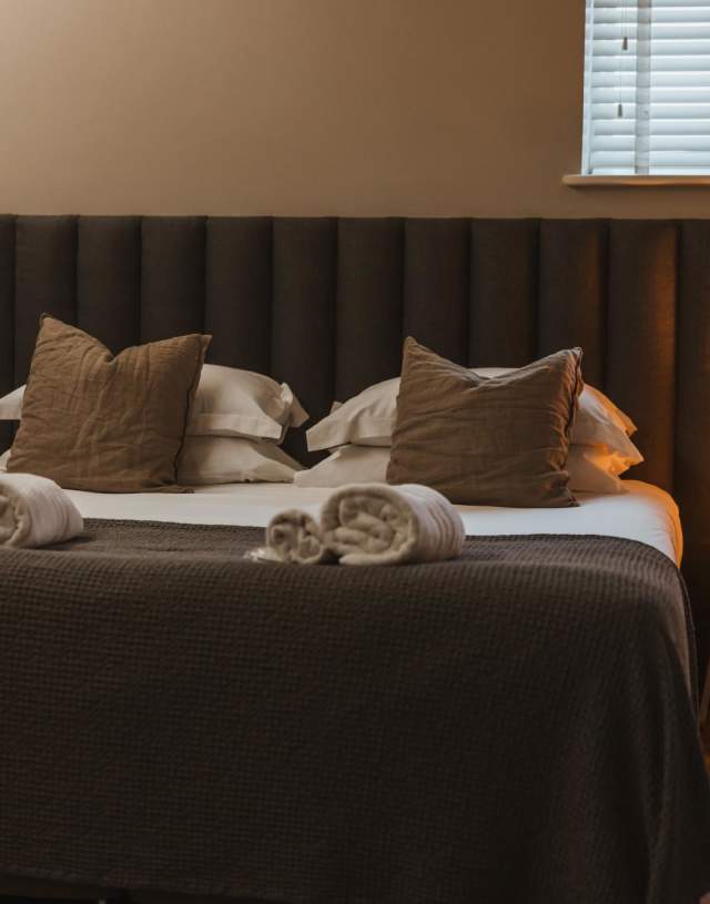 A comfy bed with grey coverings and a light on next to it.