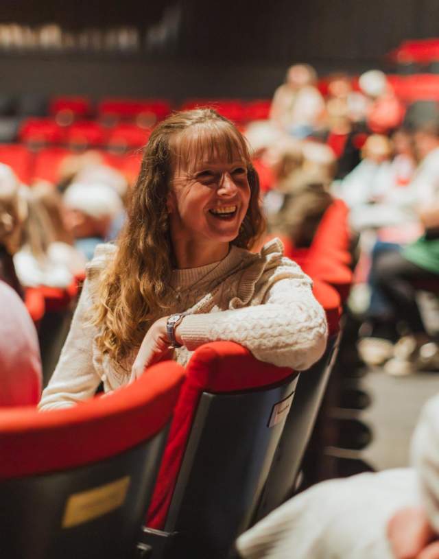 A woman has turned around in her seat whilst sat in the Hull Truck Theatre auditorium to talk to another woman sat behind her.