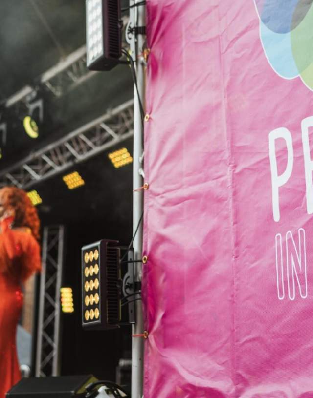 A performer in a long orange and pink dress with the stage decorated for Pride