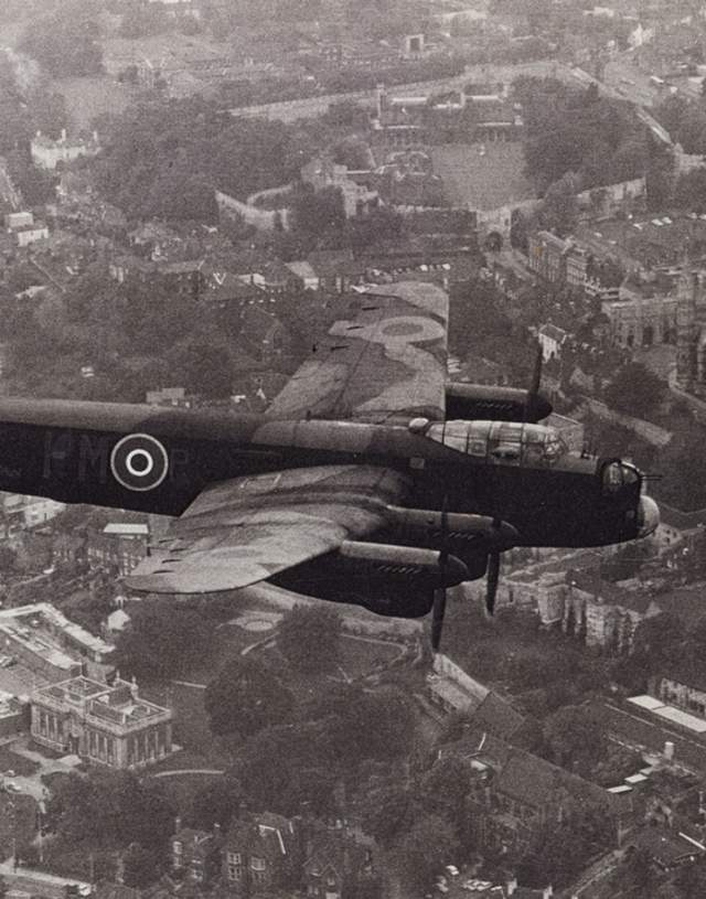 A black and white archive photo of a Lancaster Bomber flying over Lincoln Cathedral