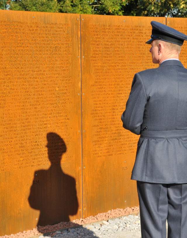 A man in military outfit inspecting a war memorial at the International Bomber Command Centre