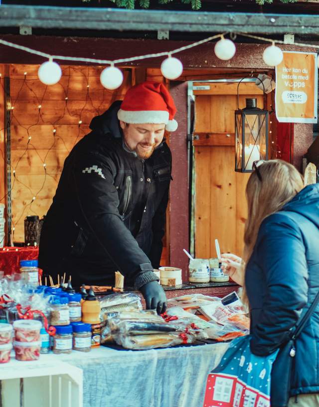 Mann som selger diverse delikatesser fra bod under julemarkedet i Sarpsborg. Foto.