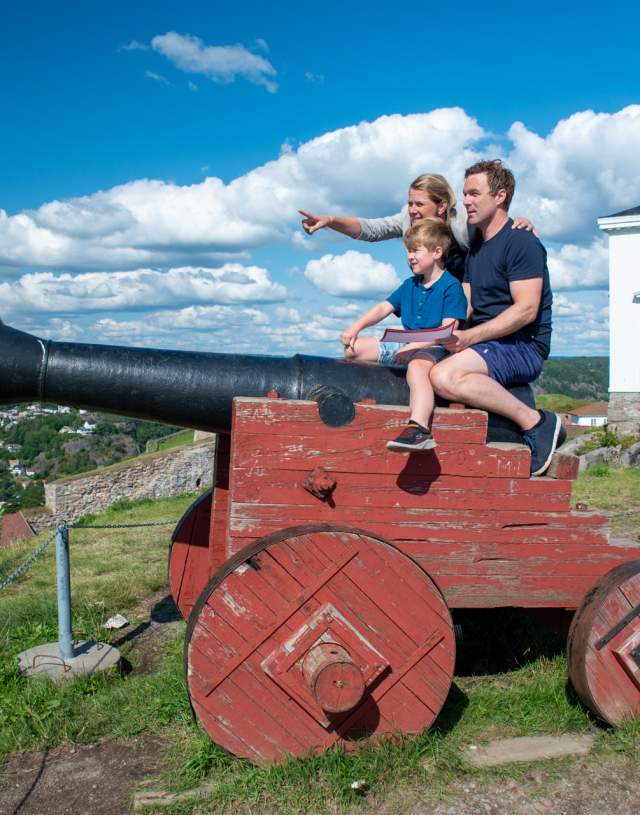 Familie som sitter på en kanon på Fredriksten festning i Halden.