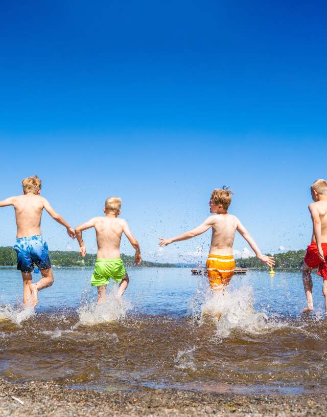 4 gutter i fargerike shorts som løper ut i vannet
