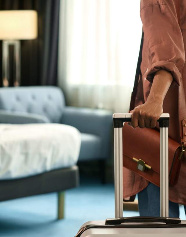 Kvinne triller kofferten sin inn på et hotellrom