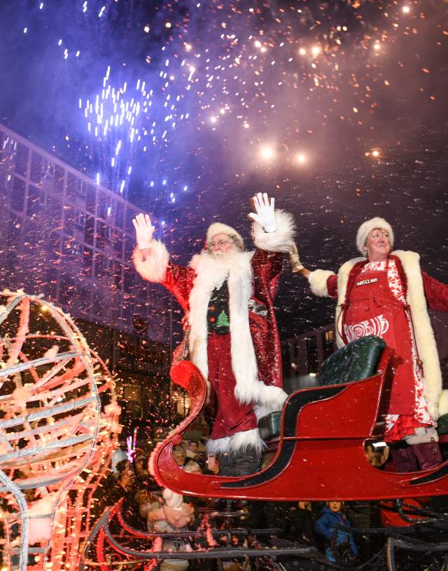 Father Christmas and Mrs Claus waving from their sleigh while fireworks go off in the swansea christmas parade