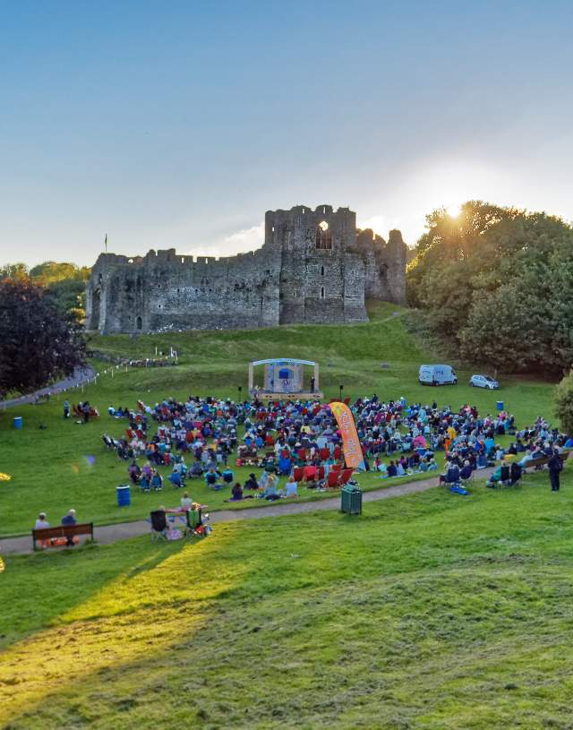theatre performance with crowd watching on with oystermouth castle in the background at sunset