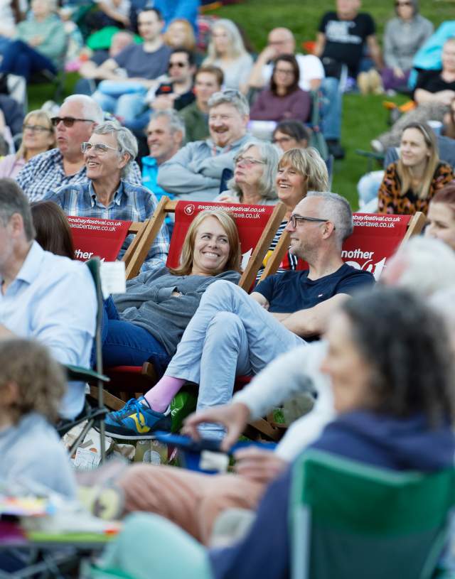 crowd sitting on deckchairs laughing and enjoying an outdoor theatre performance