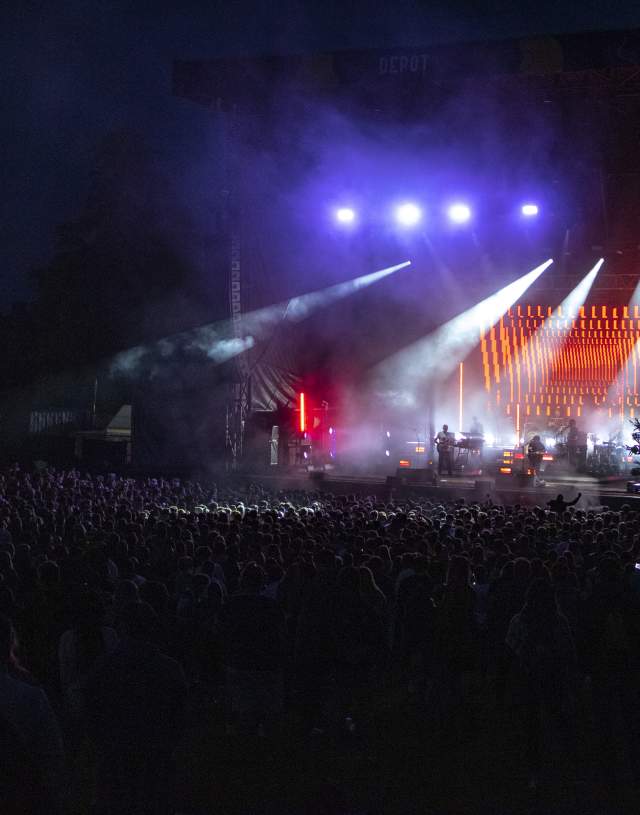 Concert stage lit up at night illuminating cheering crowds