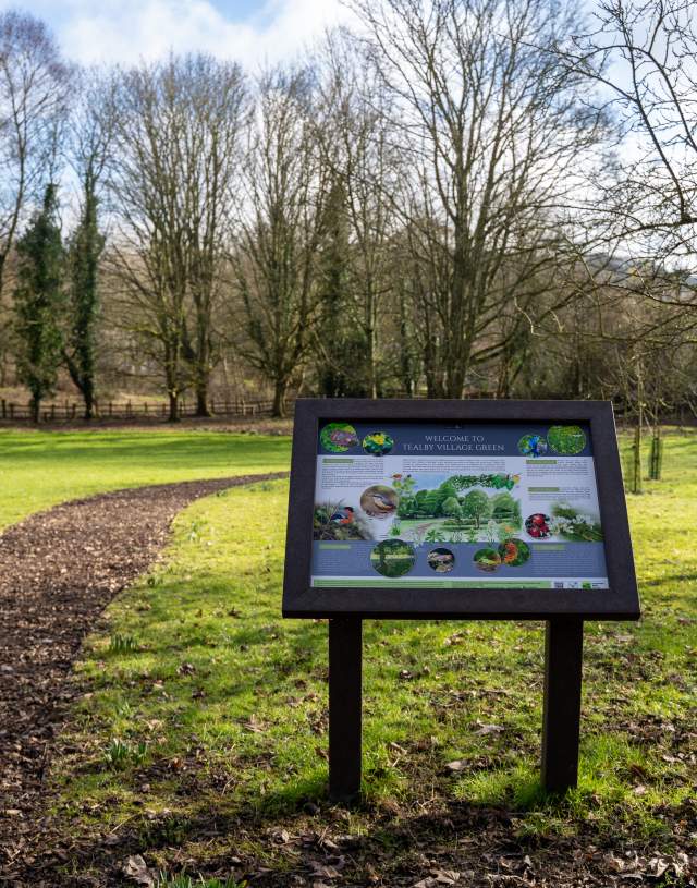 a wooden information board with fields in background on village green