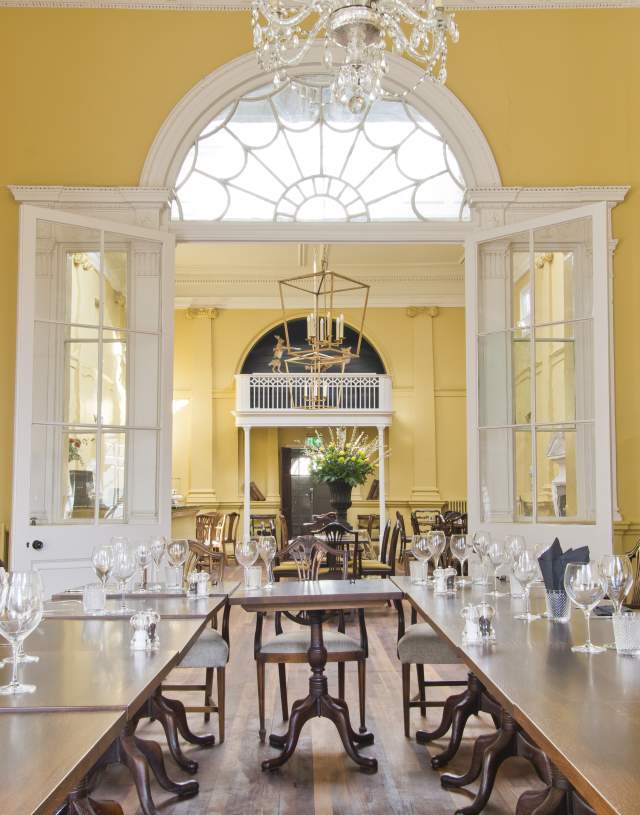 The interior of a listed buildings with yellow walls, chandelier and wine glasses on the tables