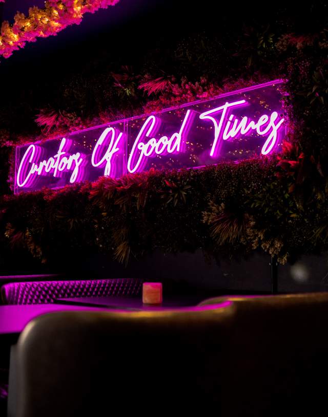 a low lit bar with neon sign on the wall reading 'curators of good times'