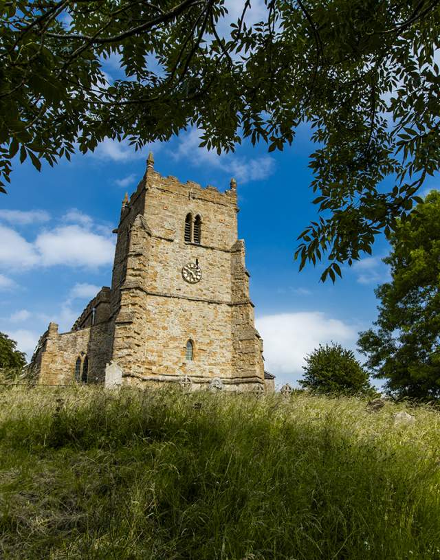 a church on a hill surrounded by trees and grass under blue skies