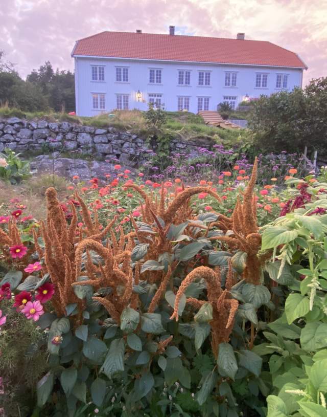 Stort, hvitt gårdshus med blomster foran