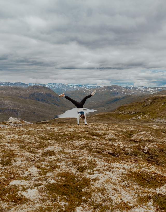 Kvinne står på hendene i fjellandskap i høstfarger
