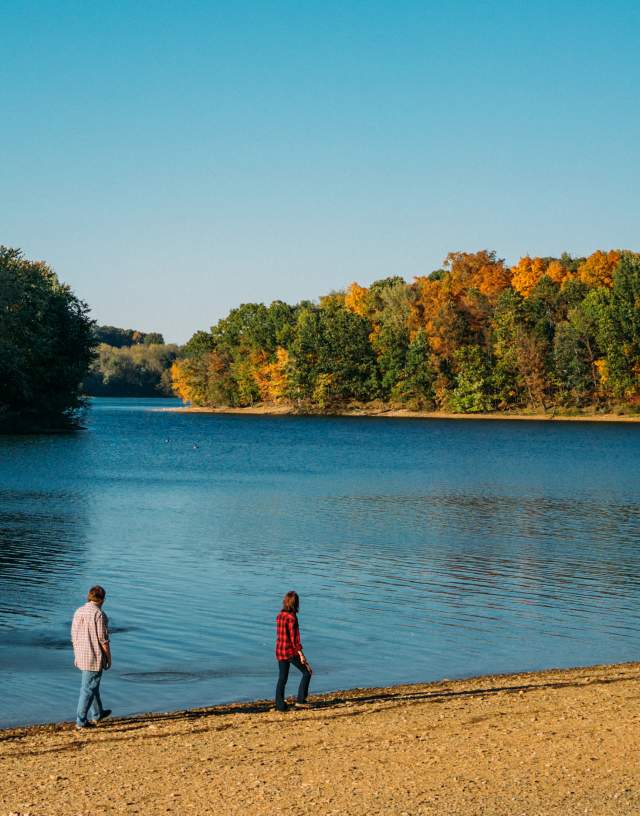 Image of two people strolling along the lake shore in fall under a bright blue sky