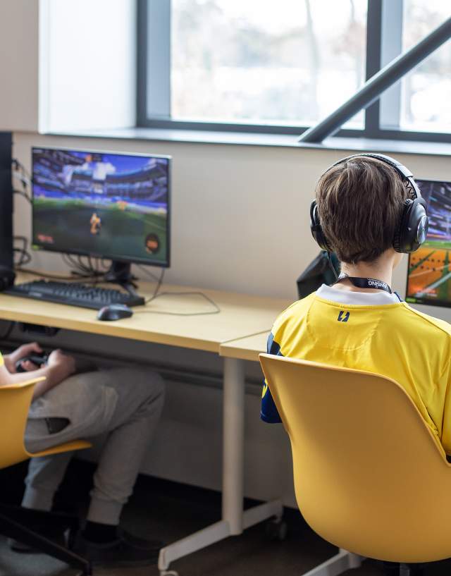 Two student competing in the MHSEL Esports Championships, each facing their own monitor and wearing headphones.