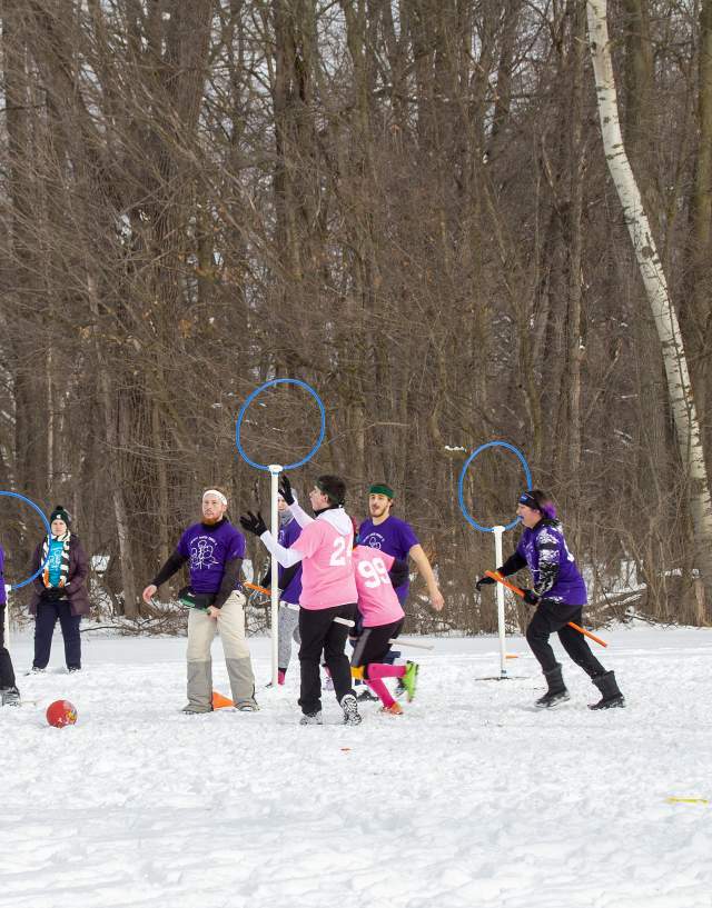Athletes playing quadball in a wooded snow-covered clearing