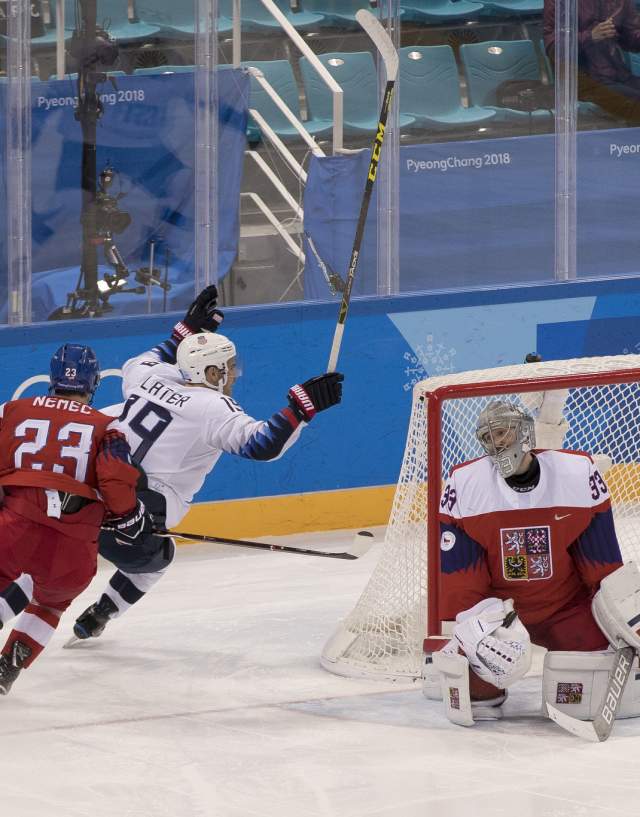 Two hockey players, one of whom is Jim Slater, skating around the goaly net with a goal tender sitting in it.