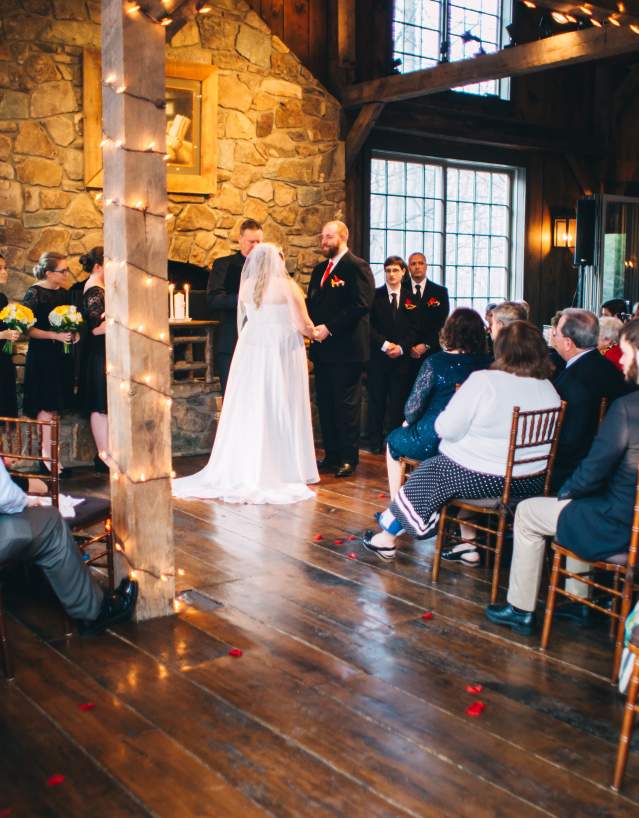 Couple saying their vows in front of a fireplace among family and friends at Thorpewood