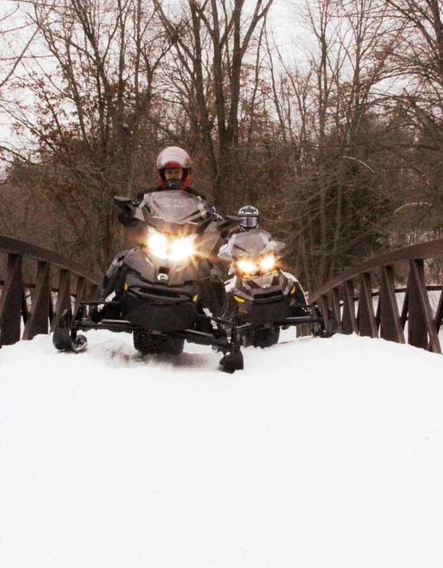 Two people snowmobiling over a bridge