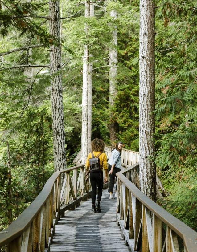Two woman walk down the forested boardwalk path.