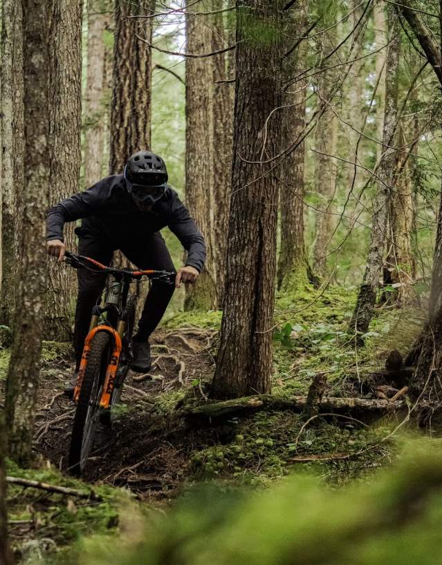 A mountain biker rides down a trail surrounded by trees and greenery.