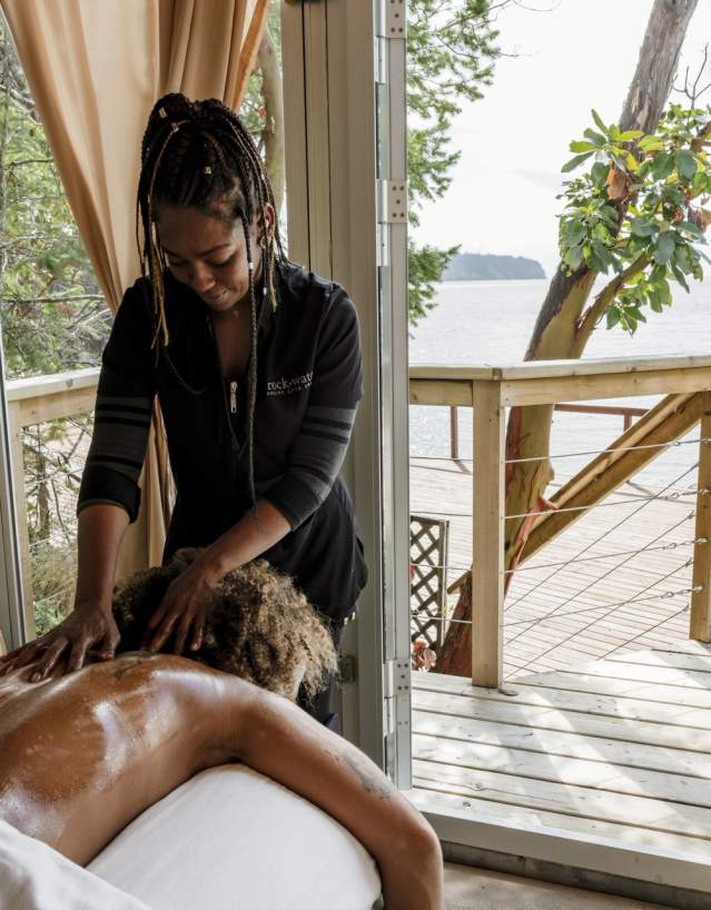 A woman enjoys a massage in a spa tent overlooking the ocean.