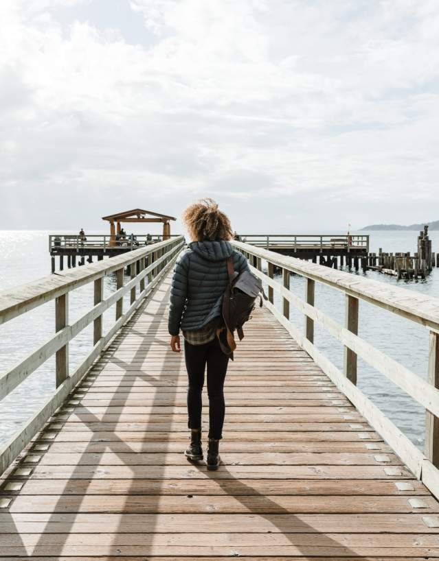 A woman wearing a backpack walks along the pier.