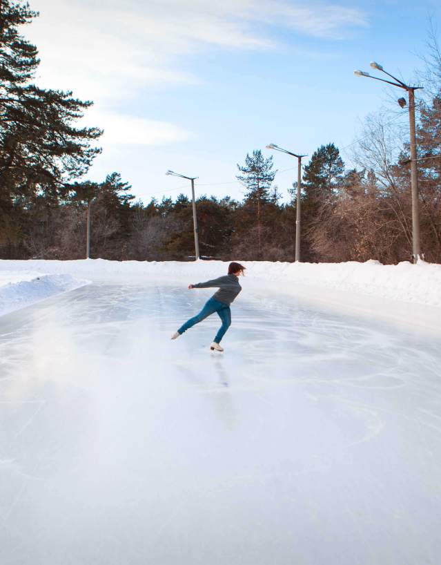 Figure skater performing on an outdoor ice rink surrounded by a snowy outdoor scene.