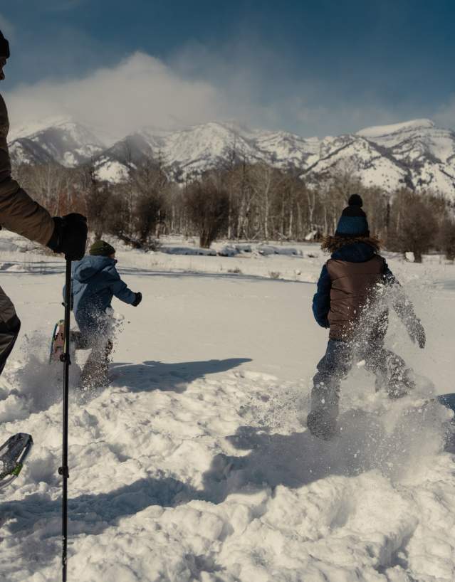 A group snowshoes through deep powder near Jackson, Wyoming, with snow-covered mountains rising across the horizon. The winter landscape and fresh snow highlight family-friendly snowshoeing and outdoor recreation in Teton County.