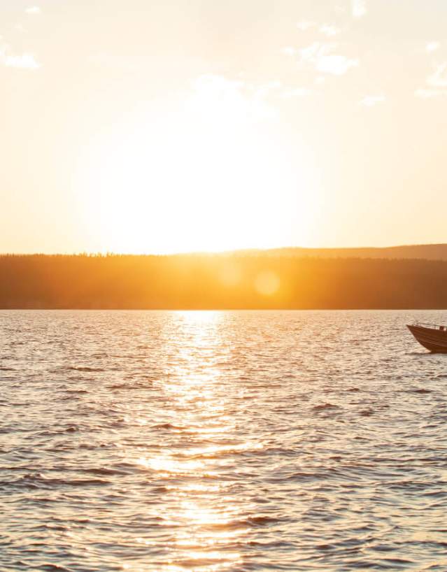 Persons boating on a calm lake at sunset surrounded by scenic mountains in Wyoming.