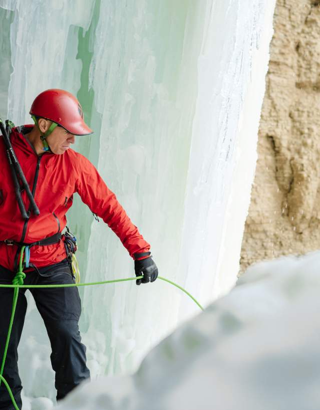 Man standing in front of frozen waterfall with climbing gear